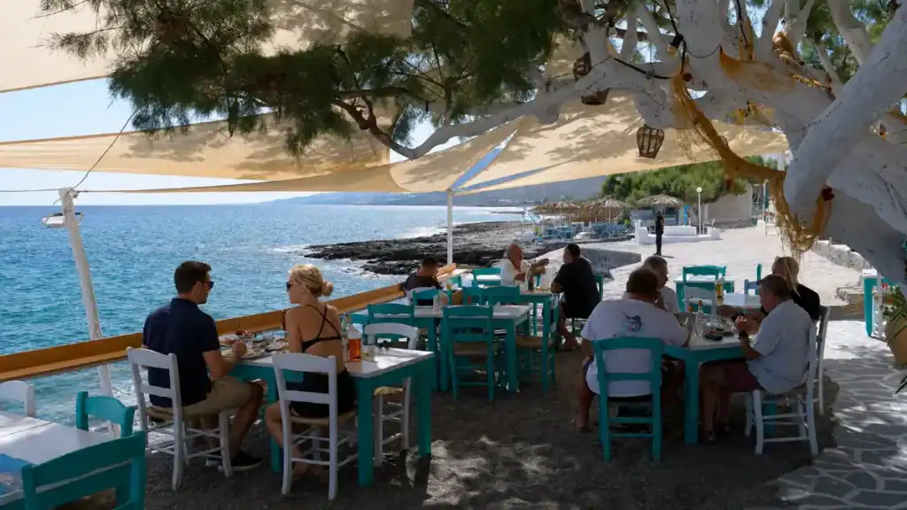 Diners at turquoise tables under shade sails at a seaside taverna in Koutsouras.