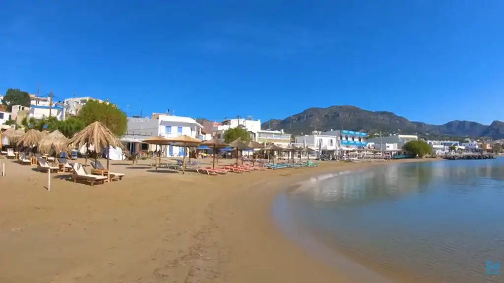 Sandy crescent shore lined with thatched umbrellas and tavernas at Makry Gialos.