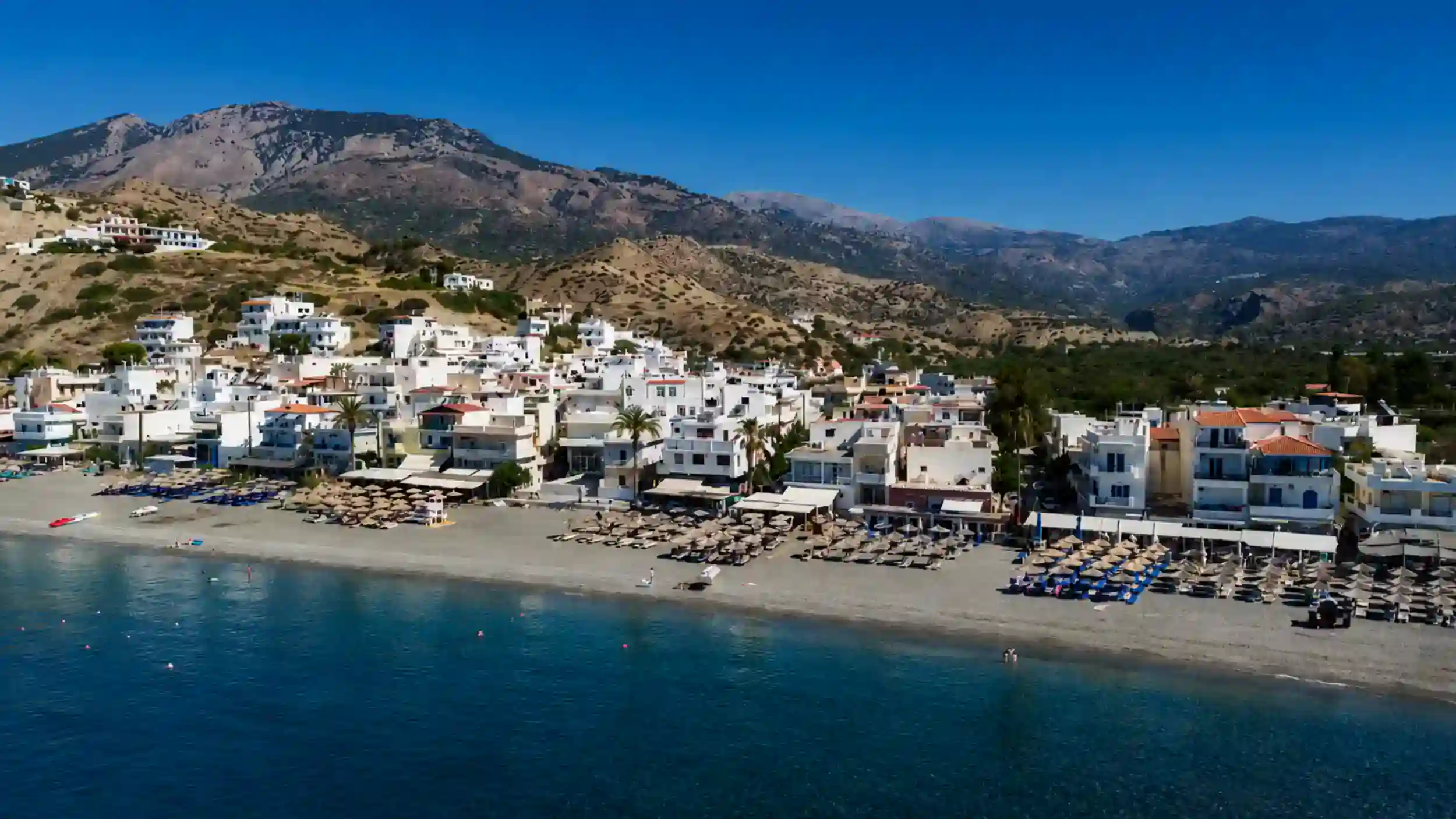 Whitewashed houses and beach umbrellas line Myrtos village on the South Coast of East Crete.