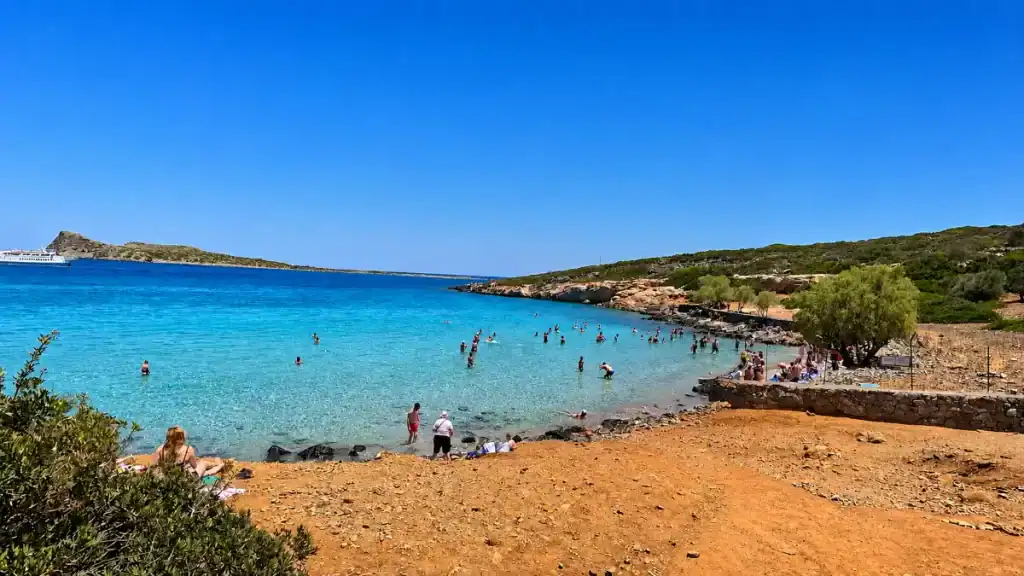 Bathers wading in shallow clear water along the sandy shore of Kolokytha Peninsula