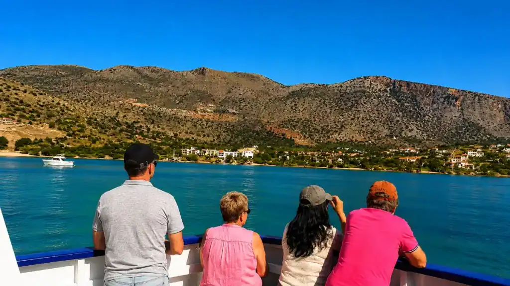 Four passengers leaning on a boat rail watching the Mirabello Bay coastline pass by