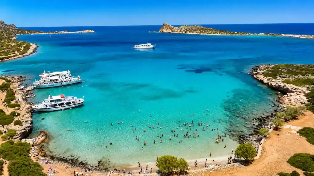 Swimmers and tour boats anchored in the turquoise cove at Kolokytha Beach