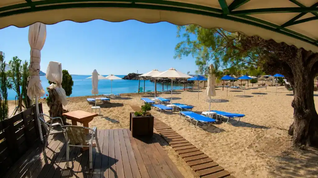 Blue sunloungers and parasols on the sandy shore at Makry Gialos beach