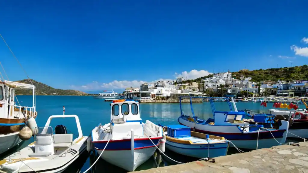 Wooden fishing boats moored at Elounda harbour with whitewashed village behind, where to stay in East Crete