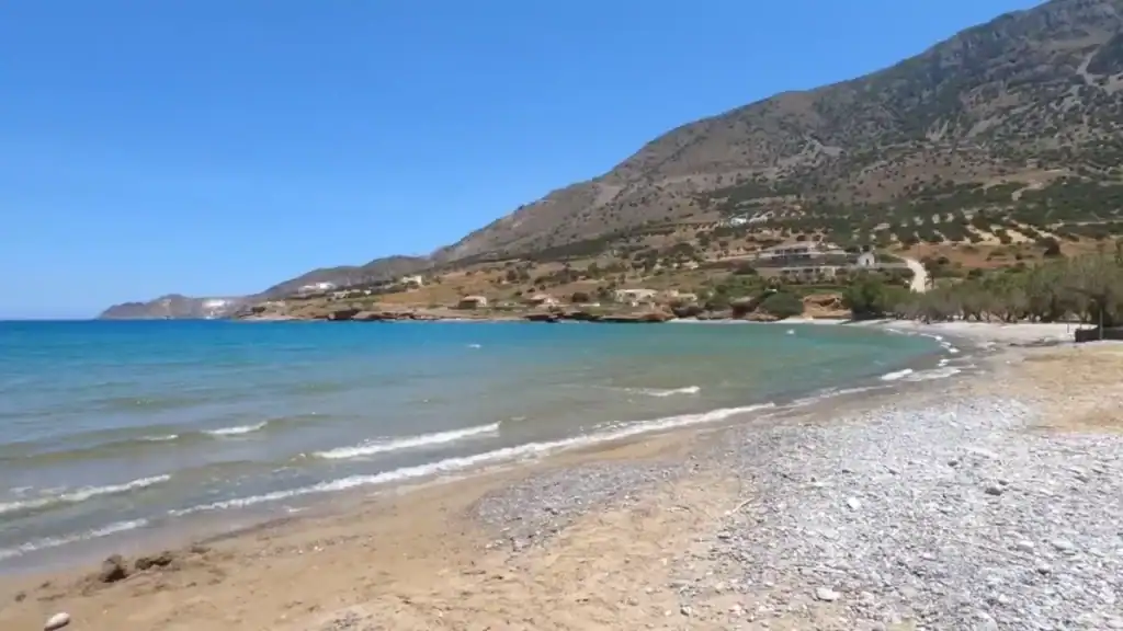 Empty pebble and sand shoreline curving below mountain slopes at Kavousi Beach