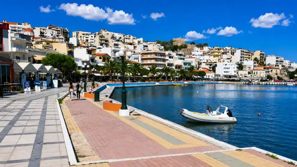 Couple walking the tiled Karamanli seafront promenade with Kazarma fortress on the hillside