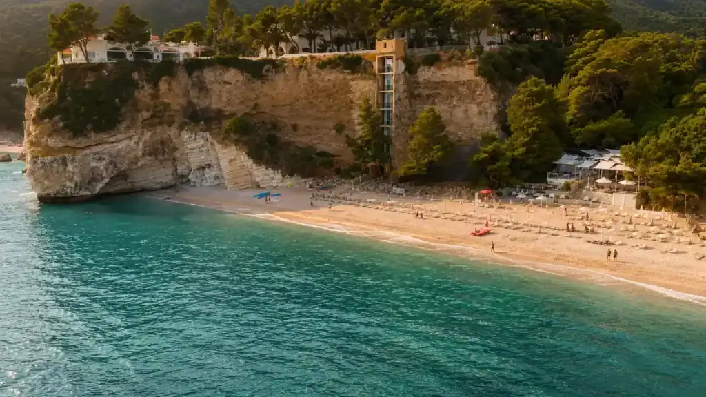 Cliffside elevator and resort terrace above the late-afternoon sands of Baia delle Zagare.