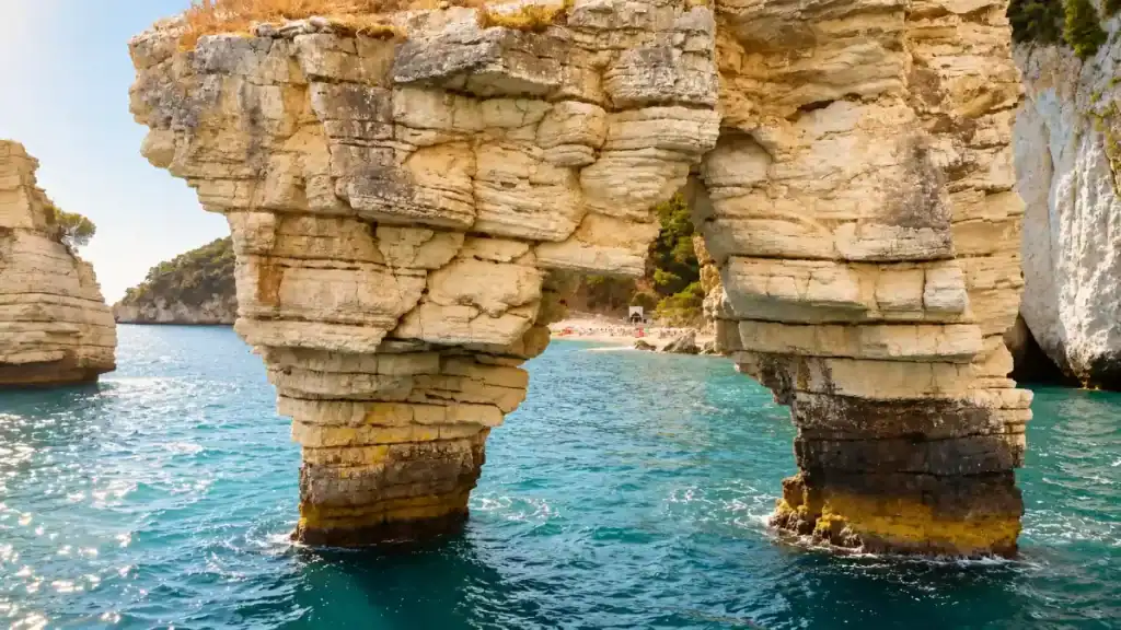 Close view through the arch of the Faraglioni di Mergoli toward a distant beach.