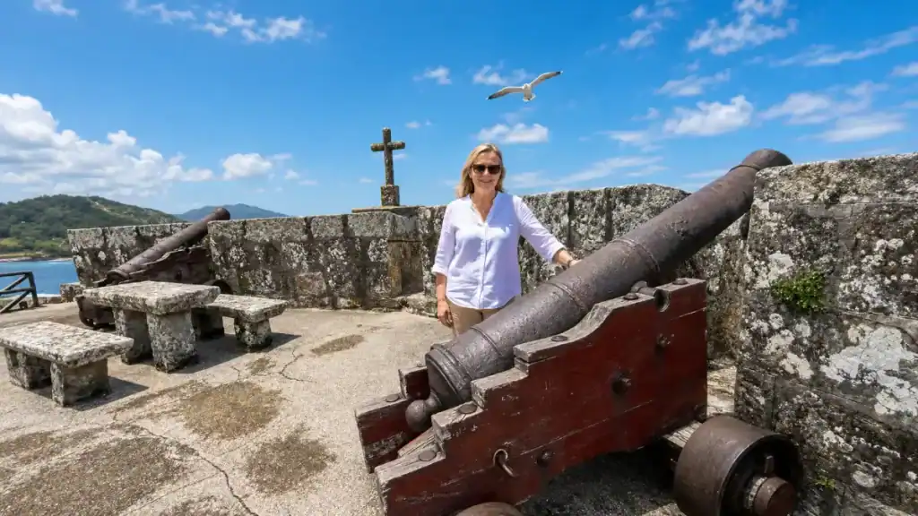 Woman standing beside an iron cannon on the battlements of Castelo de Monterreal, Baiona