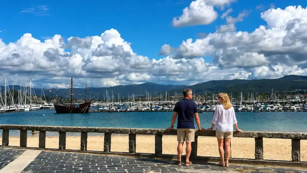 Couple looking out over Baiona and O Grove marina from a stone waterfront promenade