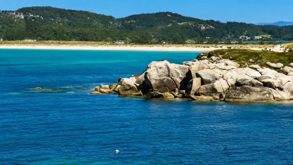 Granite boulders in turquoise water with Praia de A Lanzada's white sand strip beyond