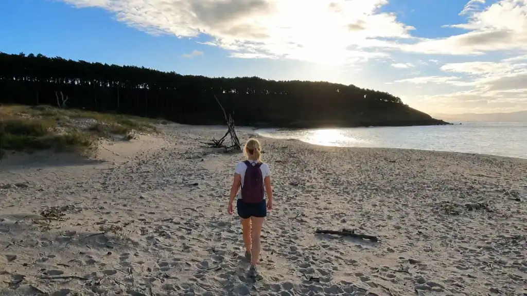 Woman walking alone on Praia de Nerga at low sun with pine-covered headland behind