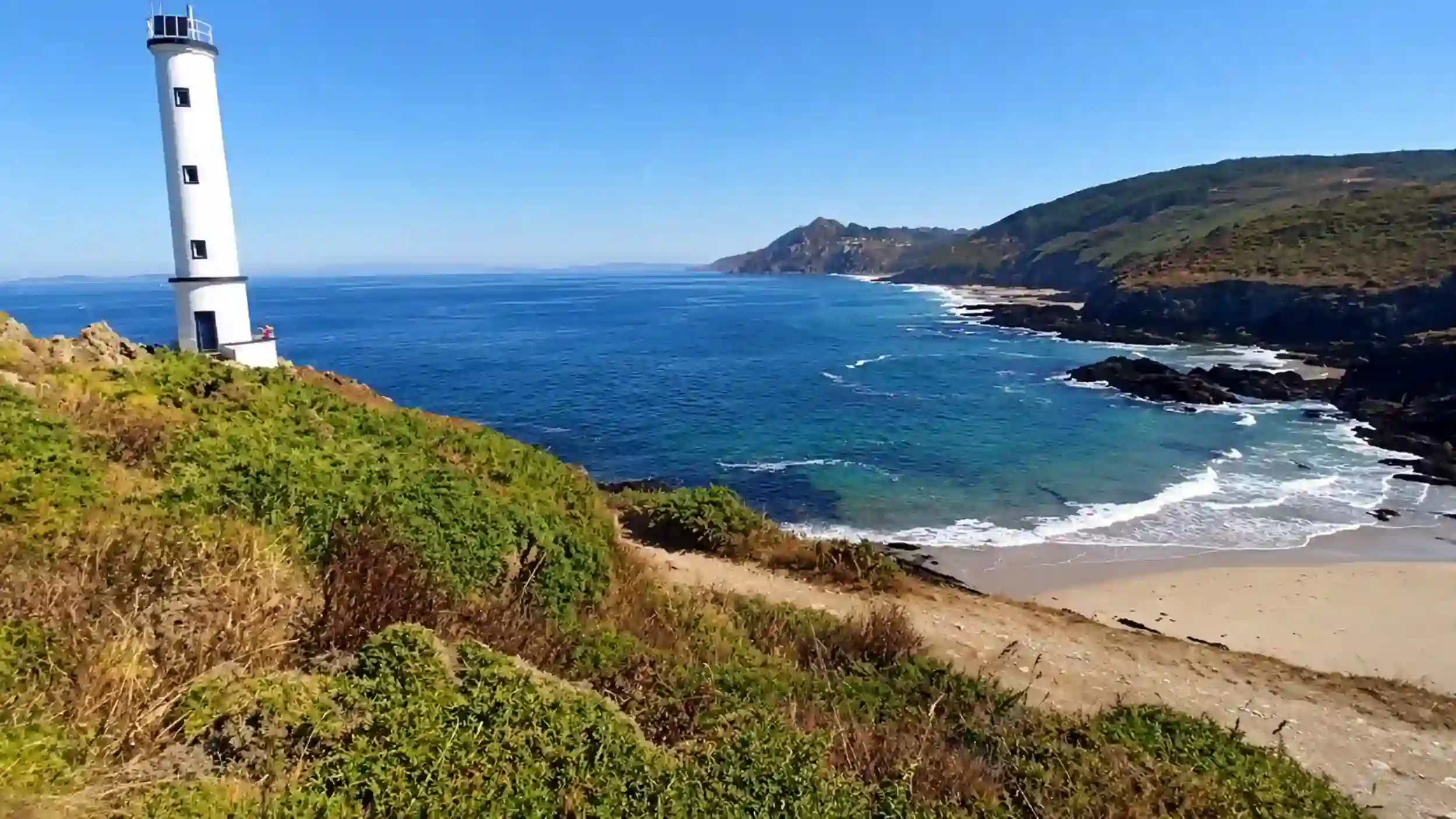 White lighthouse above a sandy cove at Cabo Home on the Galician coast