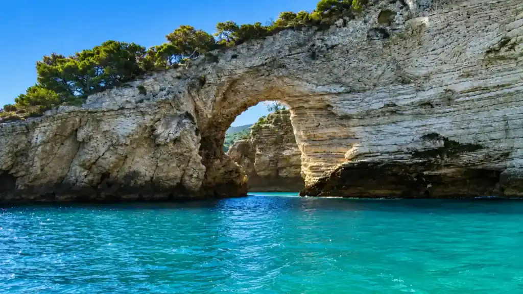 Limestone sea arch rising above turquoise water along the coastline between Vieste and Mattinata.