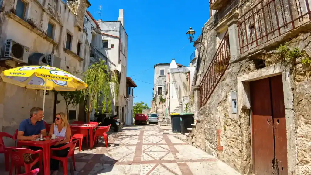 Couple having coffee at a red café table on a patterned stone street in Vico del Gargano.