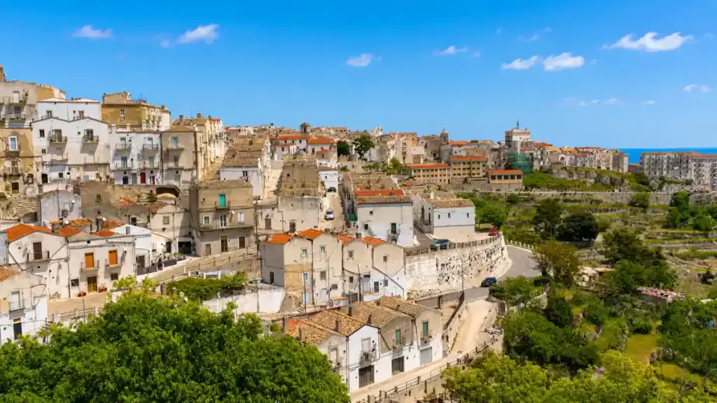 Whitewashed houses and terracotta rooftops climbing the hillside of Monte Sant'Angelo above the Adriatic plain.