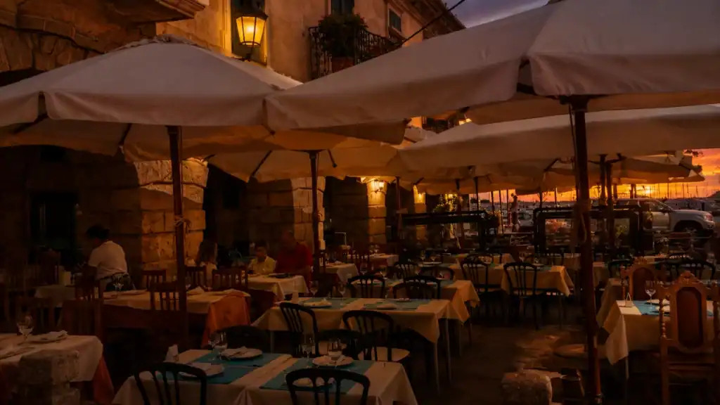 Outdoor restaurant terrace on Plaza de Castro lit by lanterns with harbour sunset beyond