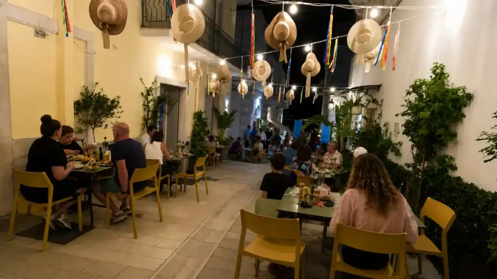 Diners seated at outdoor tables under straw hats strung above an alleyway at De Gustibus in Mattinata.