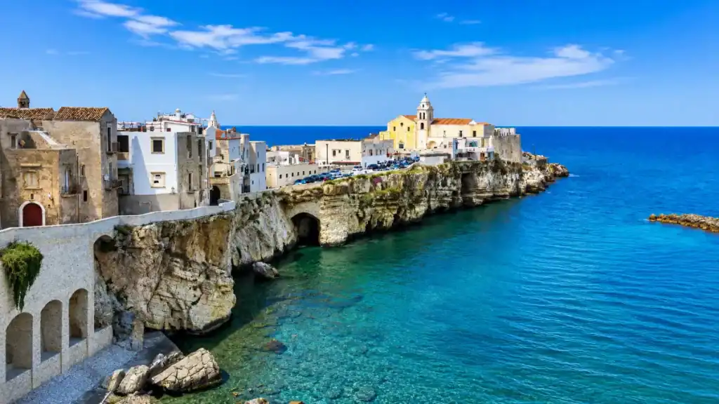 Whitewashed buildings and church perched on limestone cliffs above turquoise water in Vieste.