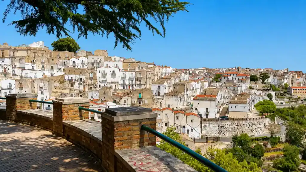 Whitewashed houses tumbling down the hillside of Monte Sant'Angelo seen from a stone terrace.