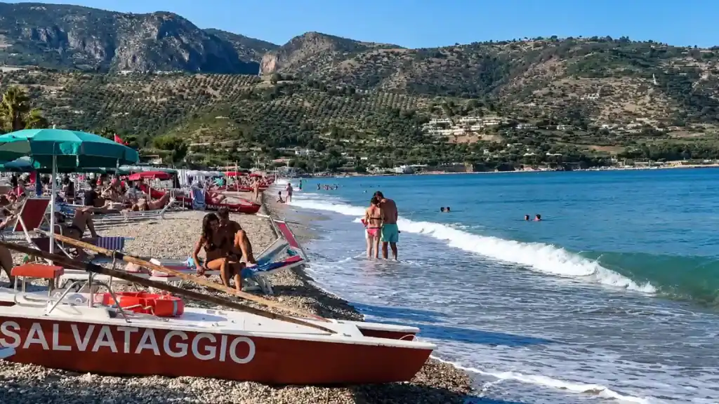Red lifeguard rescue boat on the shingle at Piana di Mattinata with olive-covered hills behind.