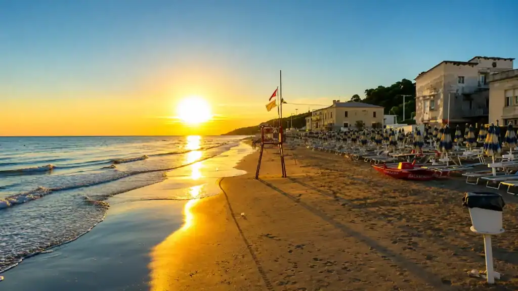 Sunrise over folded parasols and a lifeguard tower on the sand at San Menaio.