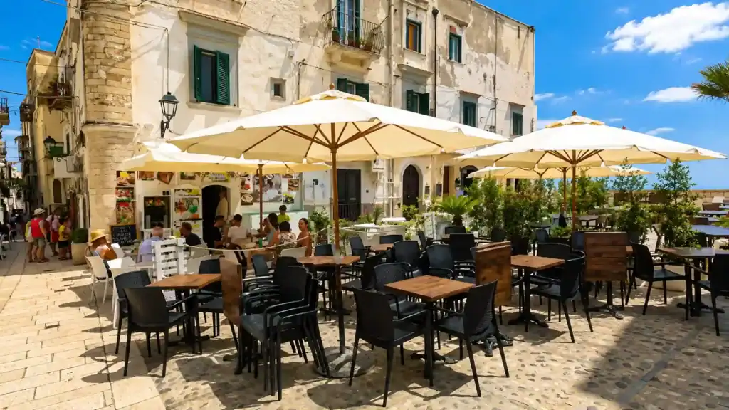 Cream umbrellas shading a café terrace in Vieste old town, Gargano Puglia beach district.