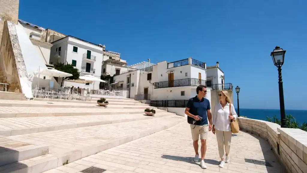 Couple walking past whitewashed houses on the Vieste clifftop promenade.