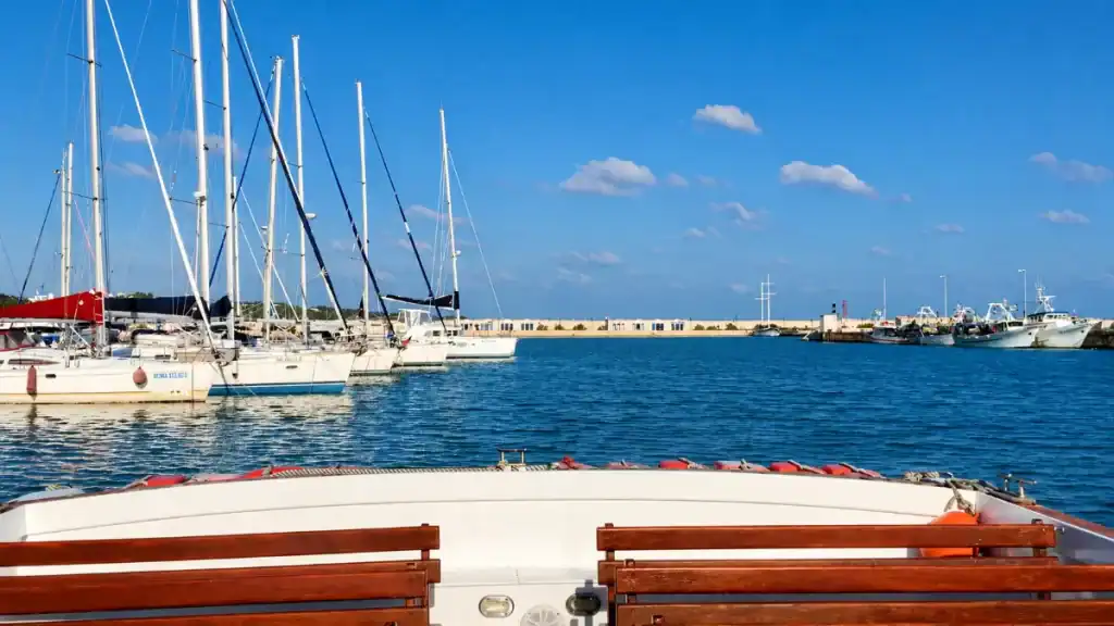 Sailboats moored along the harbour wall at Vieste marina under clear skies.