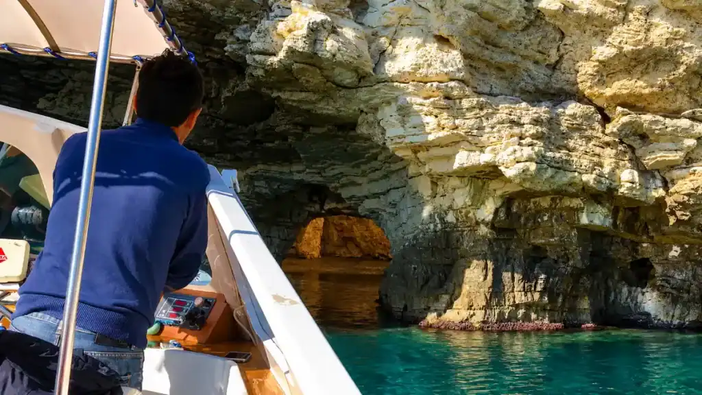 Skipper steering a small boat toward sea caves along the Vieste coastline.