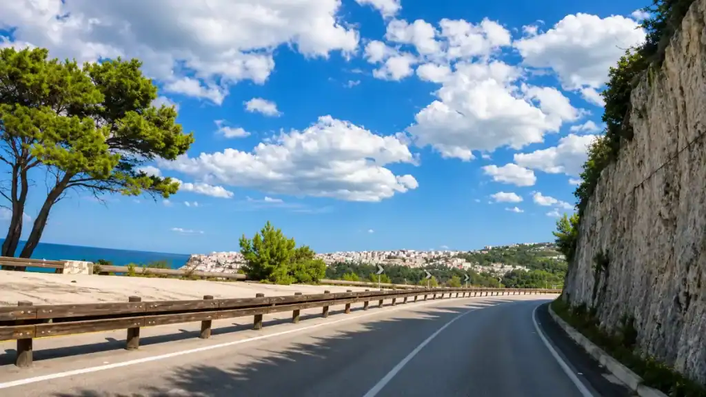 Coastal road curving toward Peschici hilltop town with limestone cliffs alongside.