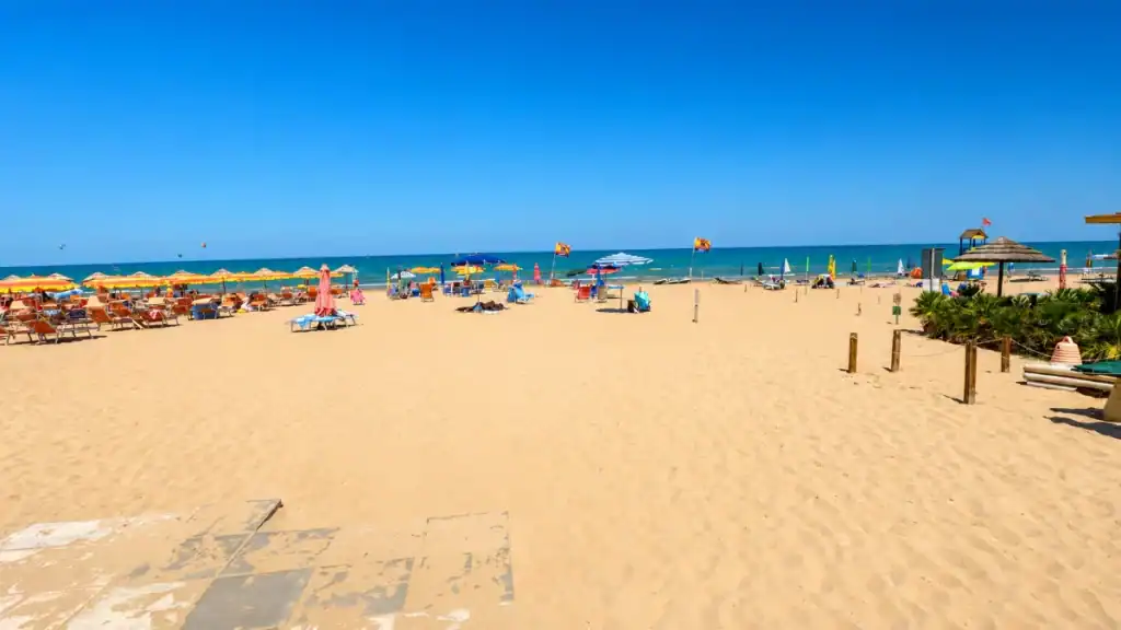 Wide sandy stretch of Spiaggia di Pizzomunno under hot midday Gargano Puglia weather.