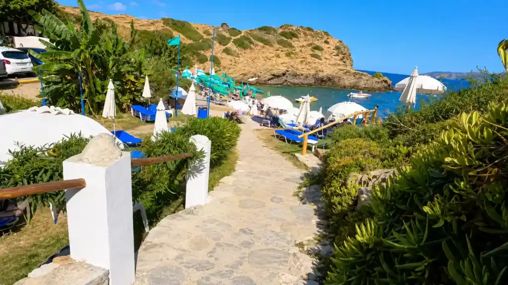 Stone pathway leading down to umbrellas and sunbeds at Karavostasi Beach.