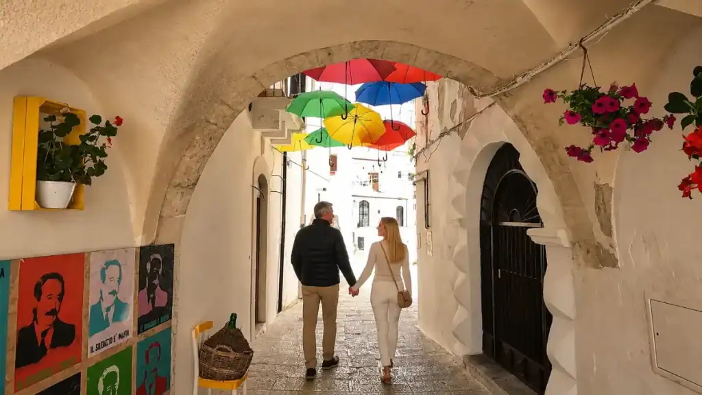 Couple holding hands walking through an arched passage with colourful umbrellas overhead.