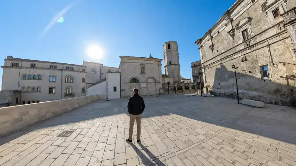 Man standing alone on Piazza San Michele facing the basilica in early light.