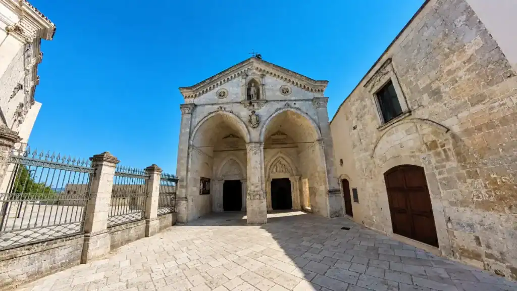 Twin-arched Gothic façade of the Sanctuary of San Michele Arcangelo under clear sky.