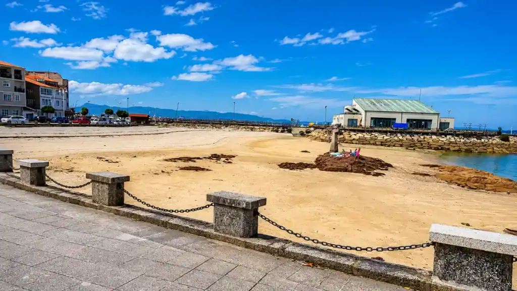 Stone-chained promenade beside a sandy cove at O Grove harbour, Galicia