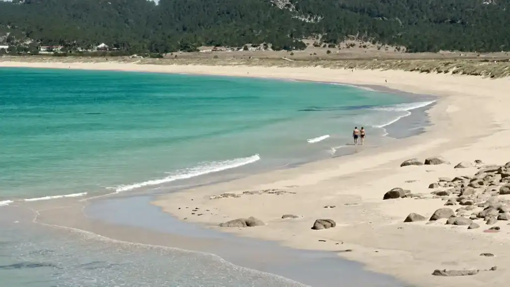 Two swimmers walking the shoreline of turquoise water at Praia da Lanzada