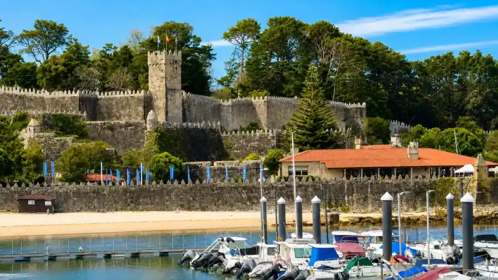 Medieval walls and tower of Castelo de Monterreal rising above Baiona's marina and moored boats