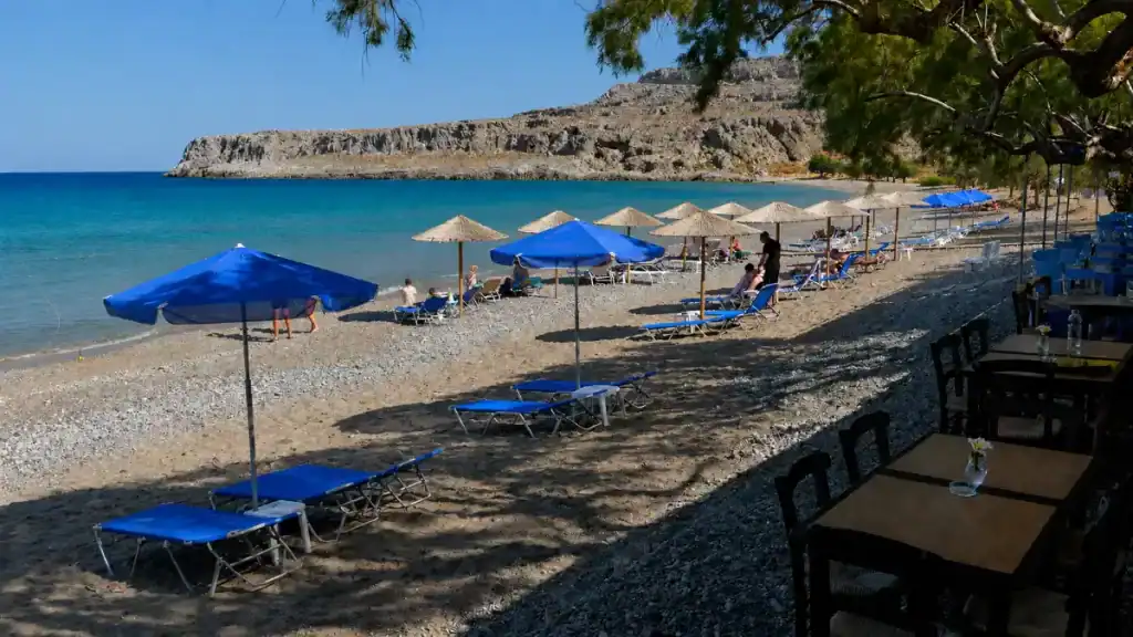 Blue umbrellas and sun loungers lined along the pebble shore at Kato Zakros Beach