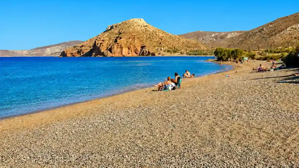 Bathers relaxing on the pebbled shoreline at Kouremenos Beach below rocky headlands
