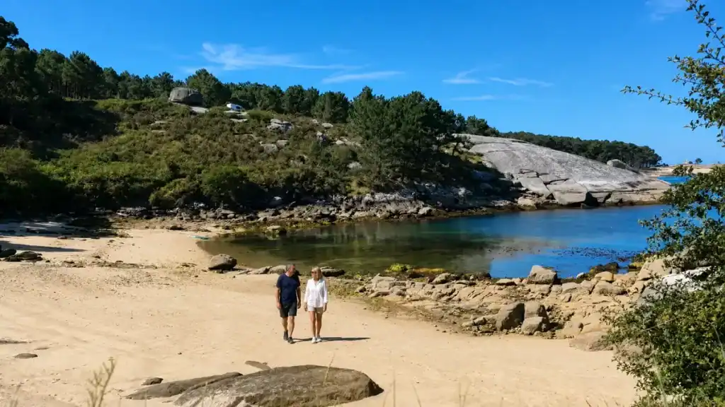 Couple walking along a quiet rocky cove on A Illa de Arousa with pine-covered granite headland