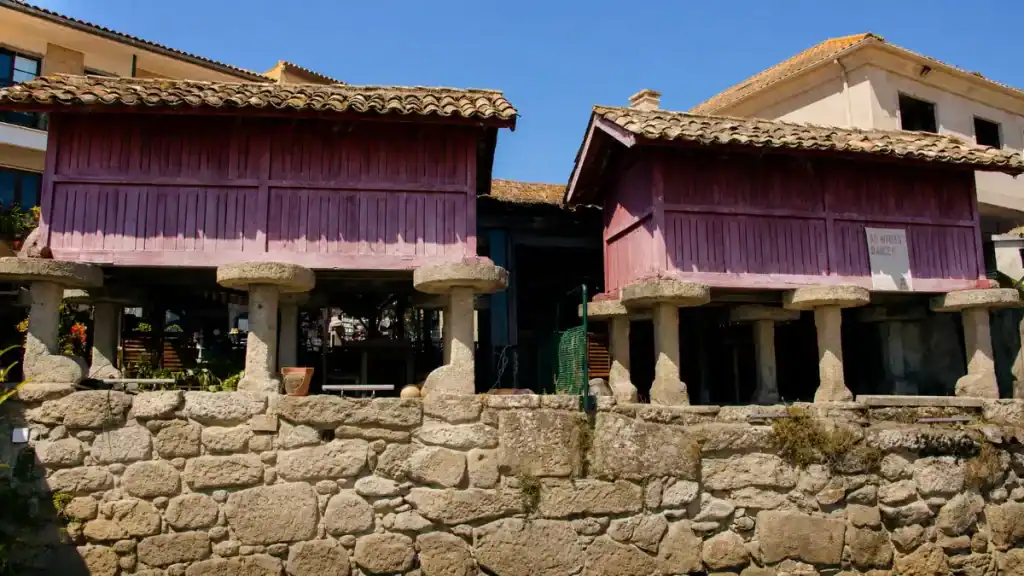 Two traditional hórreos raised on granite stilts behind a stone wall in Combarro village