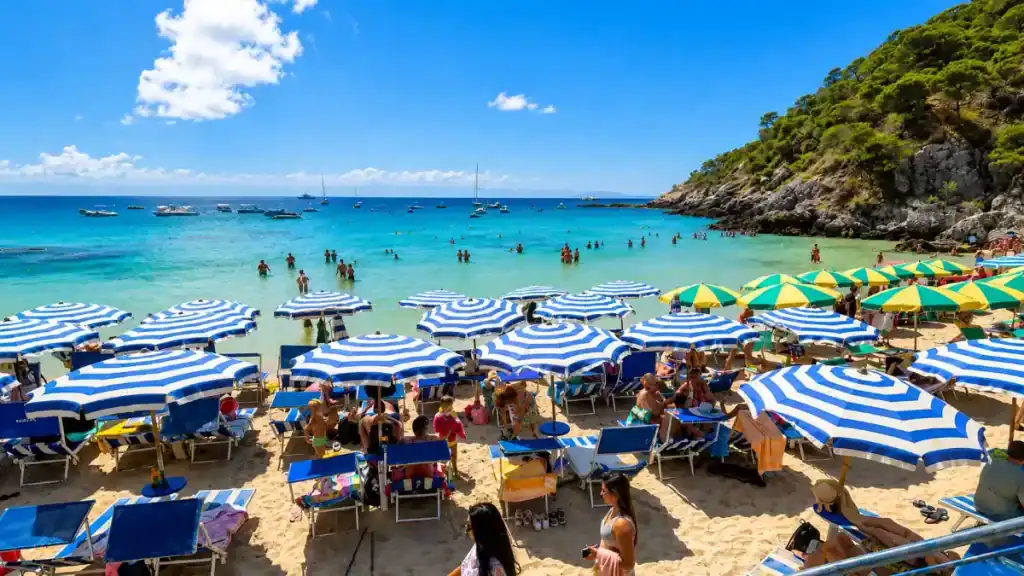 Striped umbrellas and sunbathers crowd the sand at Cala Matano in summer.