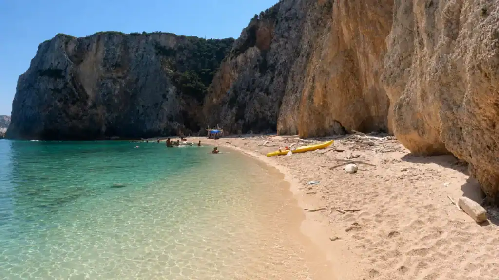 Swimmers and a yellow kayak on the sandy shore of Cala delle Arene.