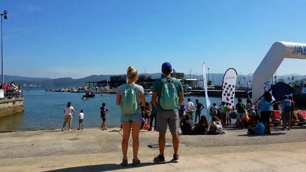 Two backpackers watching a waterfront event on the RÃa de Pontevedra harbourfront