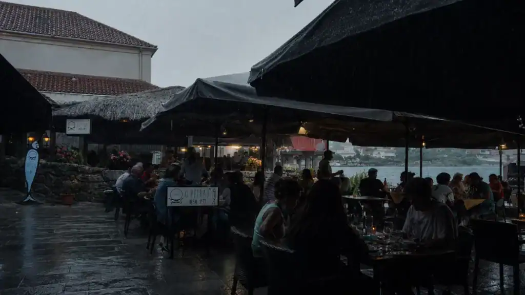 Diners sheltering under umbrellas at O Peirão restaurant on a rainy evening in Combarro to visit
