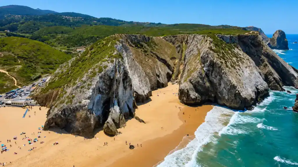 Jagged sandstone cliffs frame the golden sand of Praia da Adraga near Almoçageme.