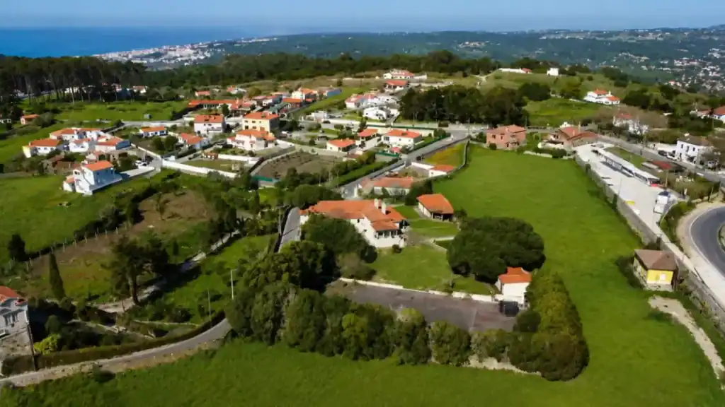 Country lane winding past quintas and orange-tiled houses near Almoçageme, with the coast beyond.