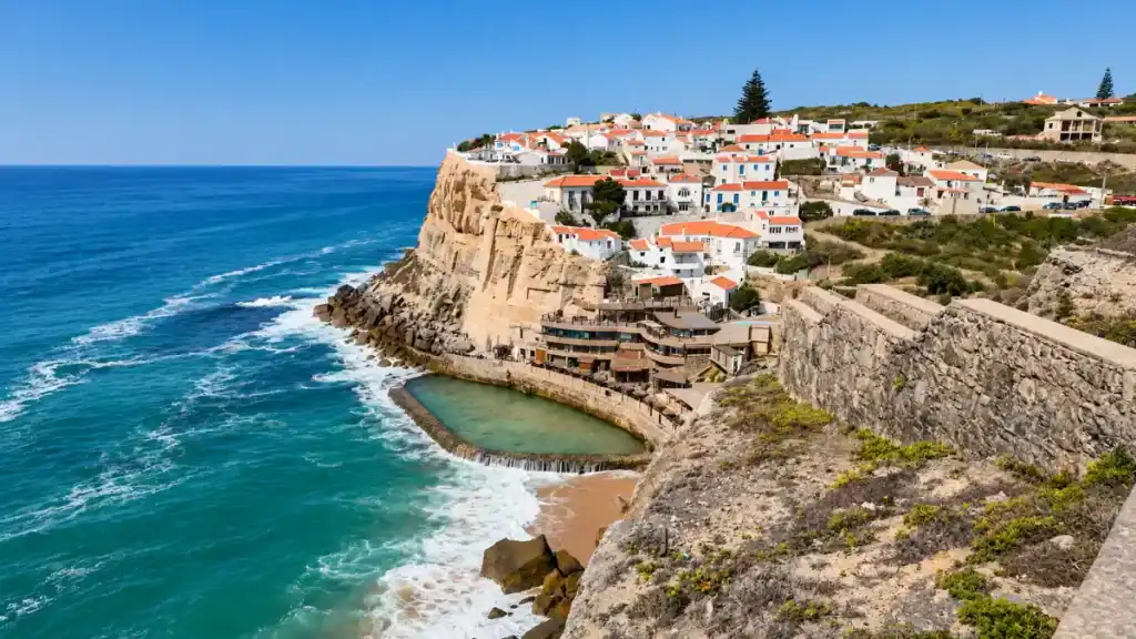 Whitewashed houses cling to clifftops above a tidal pool at Azenhas do Mar.